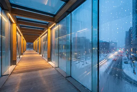 Glass pedway over a snowy downtown street at dusk